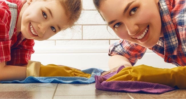 Mujer y niña sonríen mientras limpian el piso de madera
